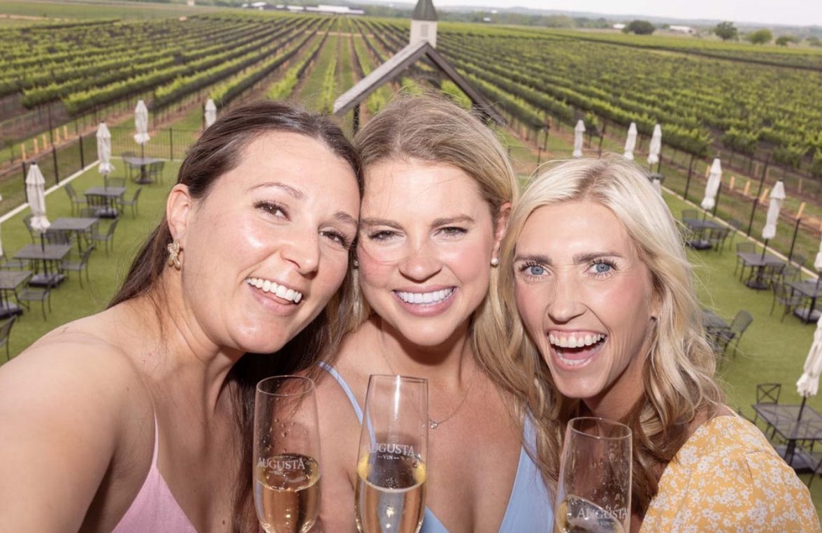 Three friends taking a selfie with glasses of sparkling wine above the vineyard rows