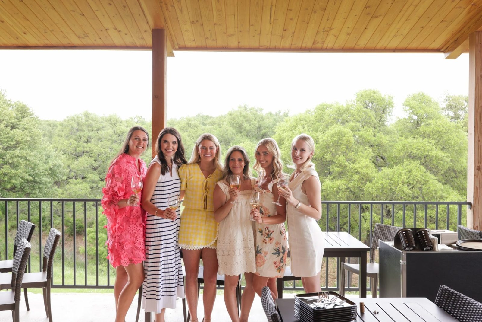 Six friends in sundresses raising glasses on a winery porch