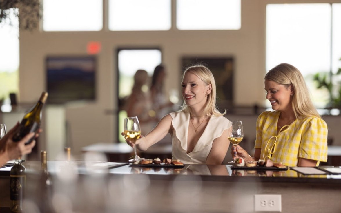 Two friends enjoying white wine and small bites at a winery tasting bar