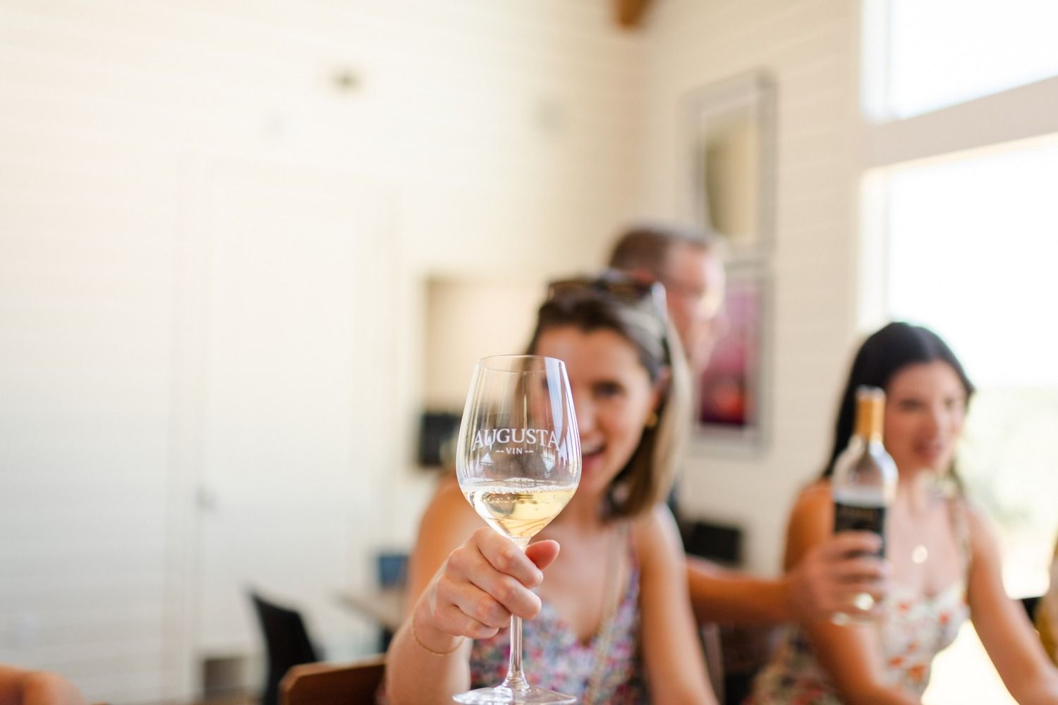 A guest raising a glass of white wine in a sunny tasting room
