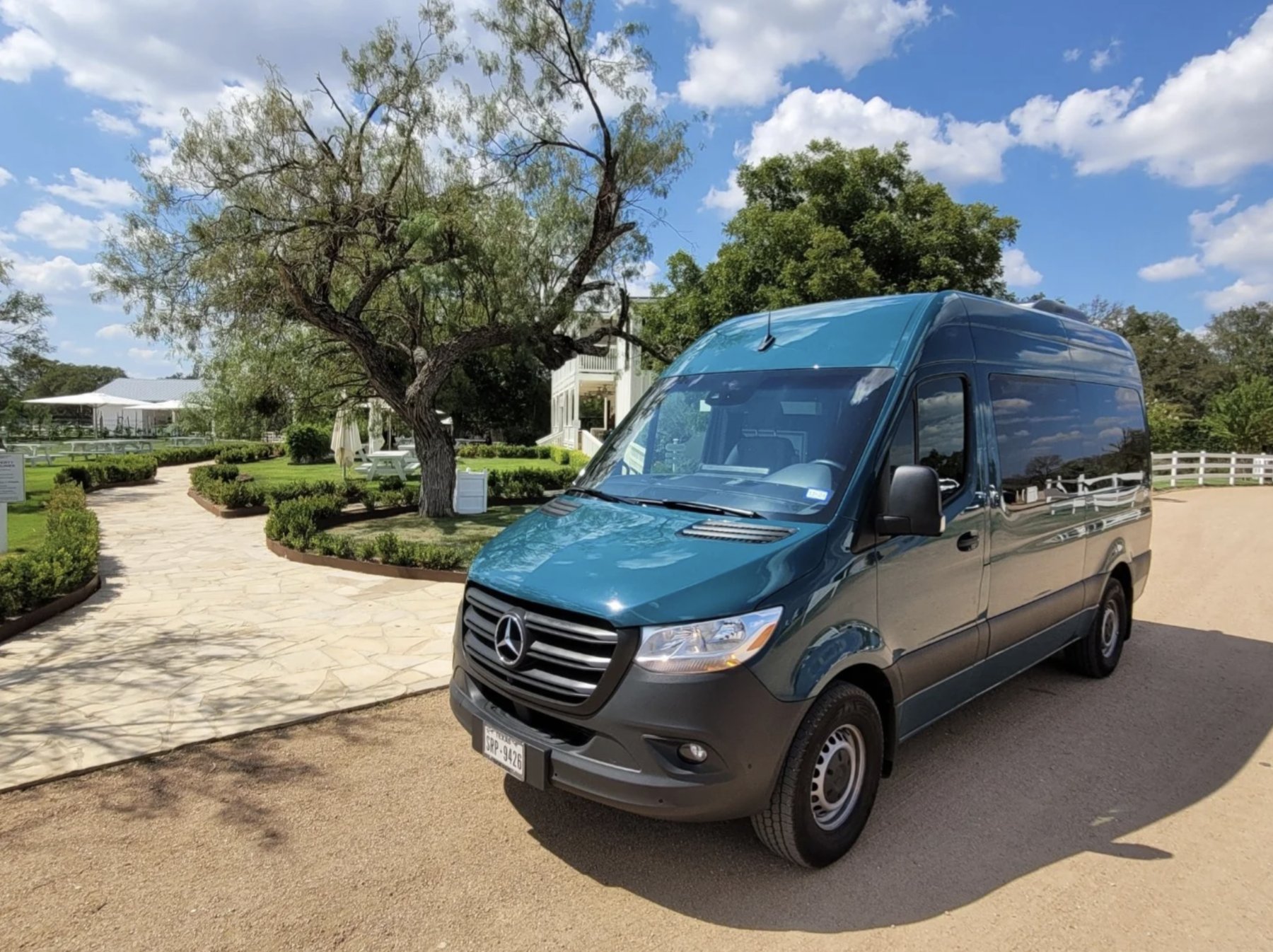 The teal Absolute Charm Mercedes-Benz Sprinter parked under the trees on a sunny Hill Country day