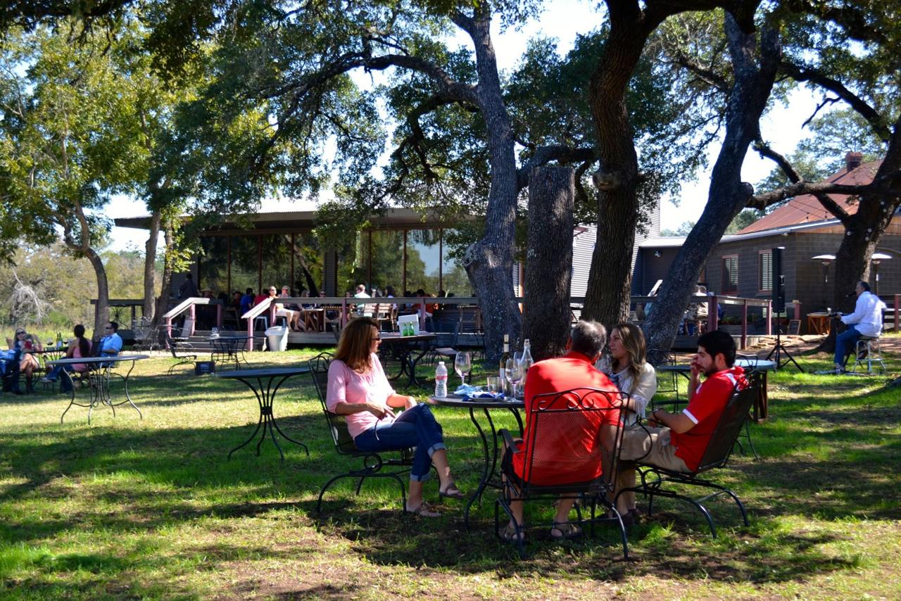 Guests sipping wine at tables under the live oaks at William Chris Vineyards in Hye